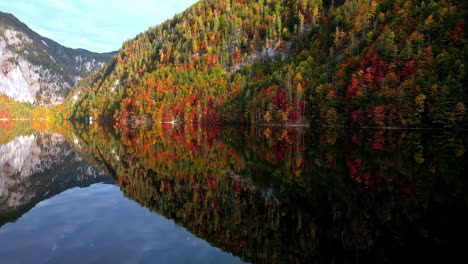 drone shot over mirroring waters of the toplitzsee lake, autumn foliage in austria