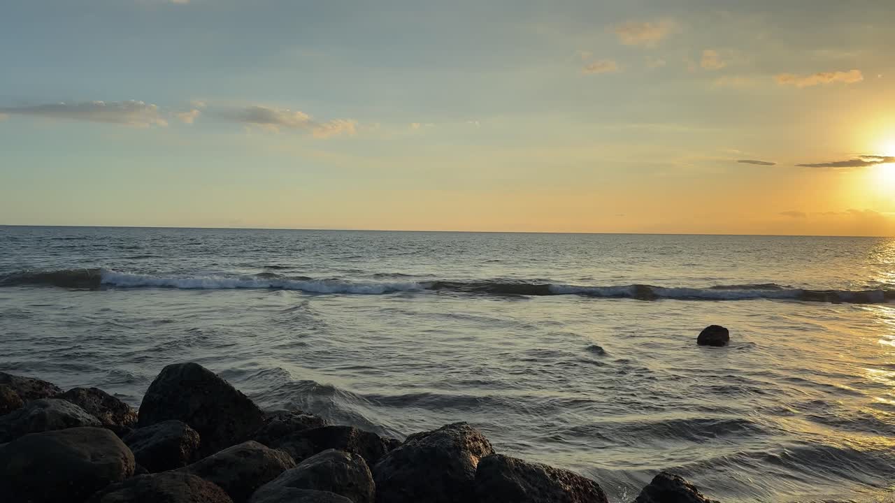 Vista Serena do Oceano com Pôr do Sol Dourado e Rochas em Primeiro Plano