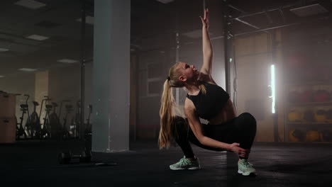 Una-Joven-Rubia-Está-Haciendo-Deporte-En-El-Gimnasio-En-Cuclillas-Y-Estirando-Las-Manos-Hacia-Arriba.