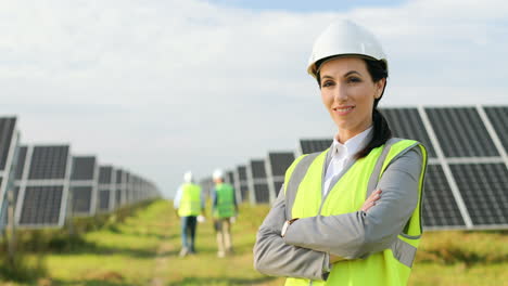 Porträt-Einer-Schönen-Ingenieurin-In-Schutzhelm-Und-Uniform-Mit-Verschränkten-Armen,-Die-Auf-Einer-Solarplantage-In-Die-Kamera-Lächeln