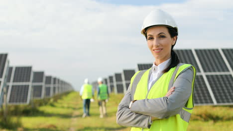 retrato de una hermosa ingeniera con casco protector y uniforme con los brazos cruzados sonriendo a la cámara en una plantación solar
