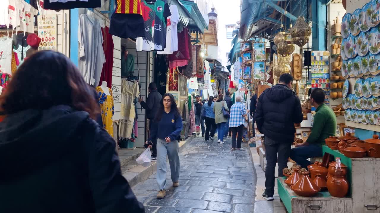 People walking through narrow alley of Medina with colorful souvenir stalls on both sides in central Tunis, Tunesia during daylight