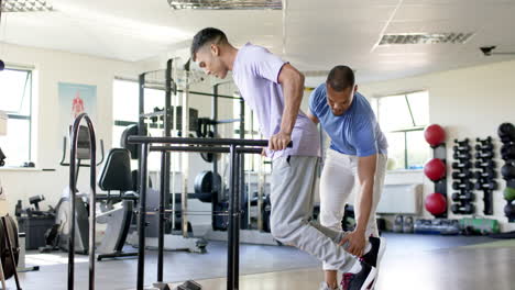 assisting with leg exercises, man supports another man using parallel bars in rehab gym