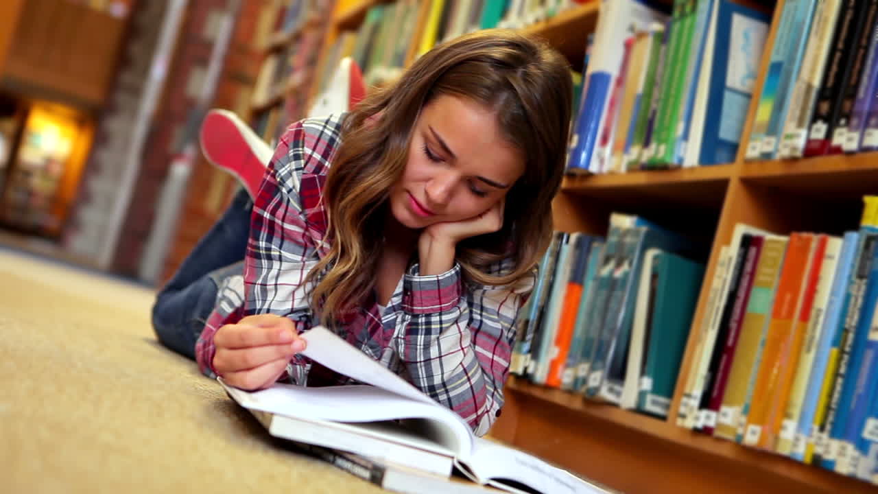 estudiante bonita acostada en el suelo leyendo un libro en la biblioteca