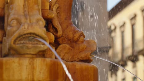 water fountain spitting water with historic sicilian buildings in the background, catania, sicily