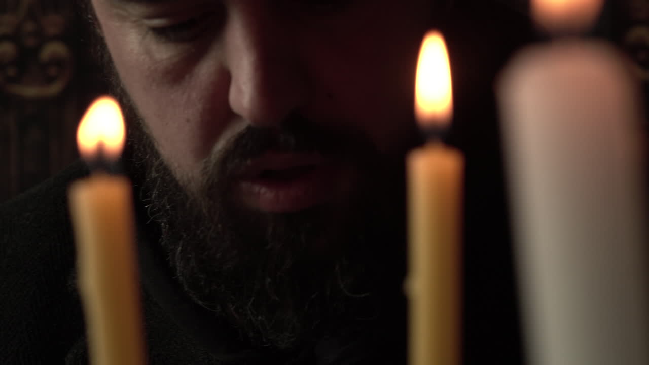 Sacerdote cristiano che legge la Sacra Bibbia davanti alle candele, primo piano