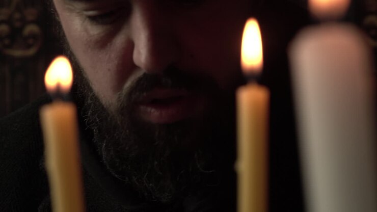 Christian Priest Reading Holy Bible in Front of Candles, Close Up