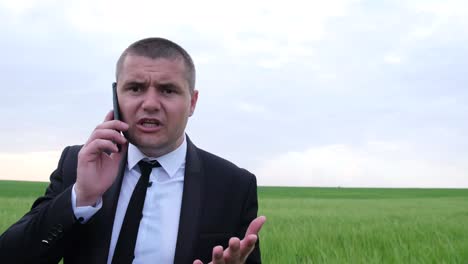 an agronomist in the middle of a green field he is talking on a smartphone in a business suit an agronomist in the middle of a green field he is talking on a smartphone in a business suit businessmen quarrel over the phone the concept of anger and rage