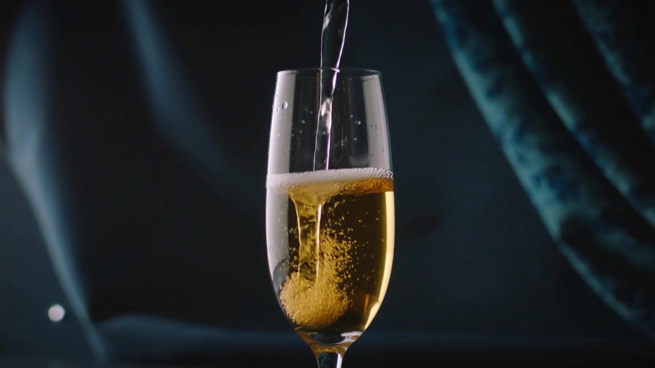 Versando un sottile getto che entra in un flûte da champagne in uno studio buio, creando bollicine dorate e goccioline.