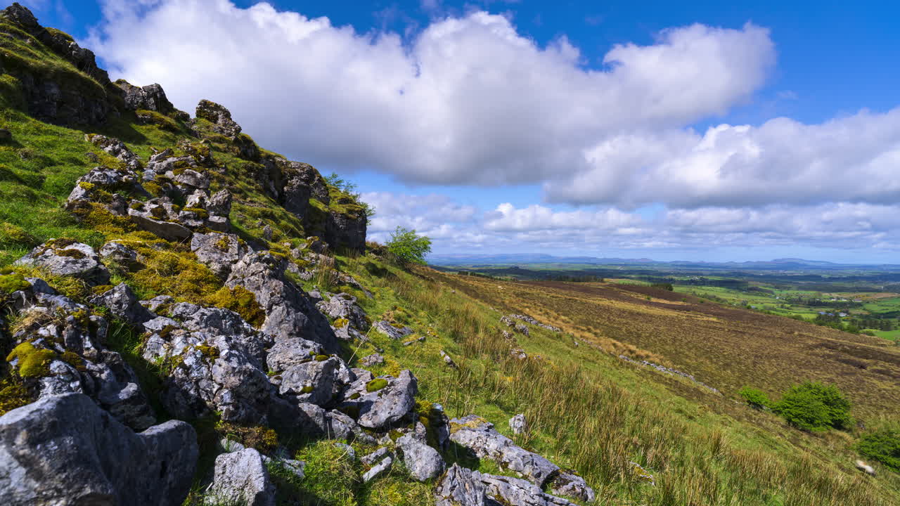 Timelapse af et landligt landskab med en klippeformation i forgrunden og bakker i det fjerne på en solrig og skyet dag, set fra Carrowkeel i County Sligo i Irland
