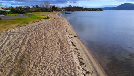 Drone-shot-along-the-empty-grassy-sandy-shore-with-tire-tracks-and-gentle-waves