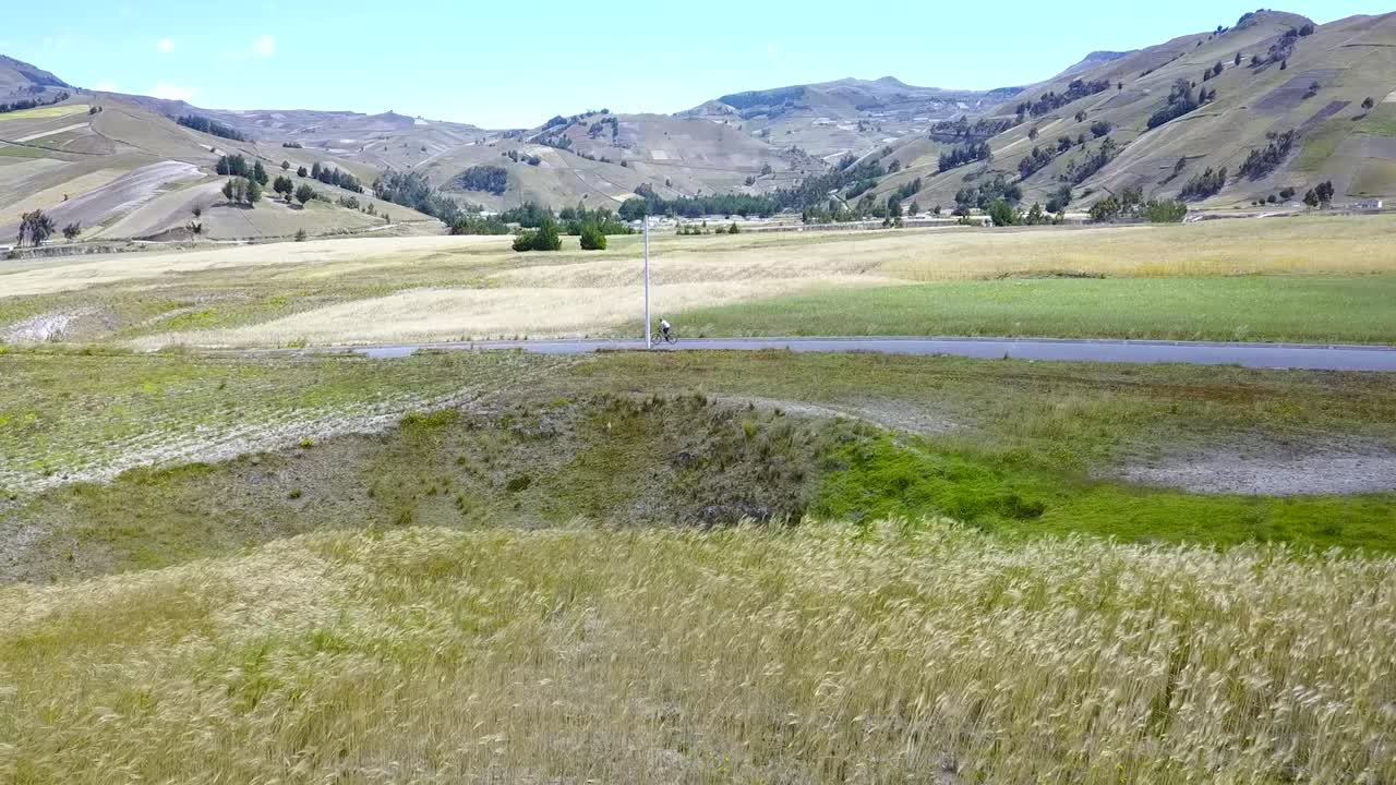 ciclista en bicicleta pasando por campos rurales y montañas en un día soleado en quilotoa, ecuador