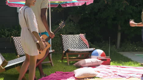 Diverse friends enjoying sunny day by pool, playing guitar and relaxing with drinks