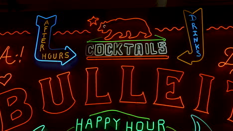 black bar wall with led signs advertising cocktails and happy hour