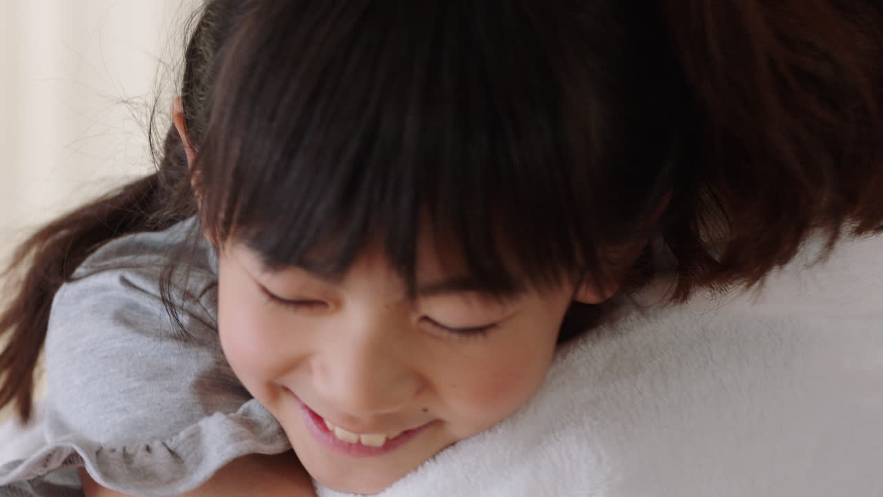 幸せな小さなアジアの女の子が母親を抱きしめ 笑顔で娘を抱きしめ 母の愛を楽しんで 可愛い子供が母親に抱きしめ 家庭で愛情を示す 家族のコンセプト 4k映像