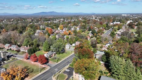 american neighborhood with main street and driving cars. picturesque landscape with colored trees in foliage fall season. aerial orbit top down shot. wide shot.