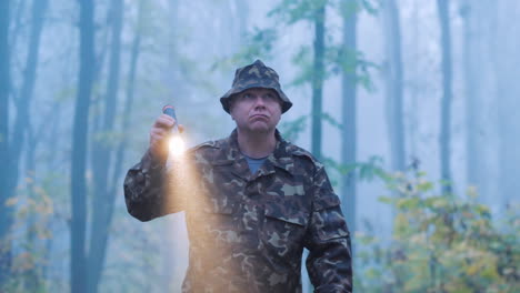 a man with a flashlight in his hand walks through the forest in the fog