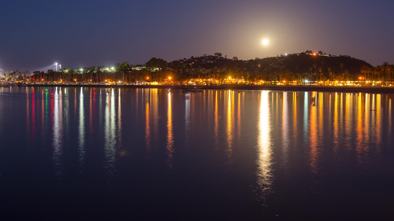 lapso de tiempo de una puesta de luna llena y barcos que salen del puerto de santa bárbara al amanecer en santa bárbara california