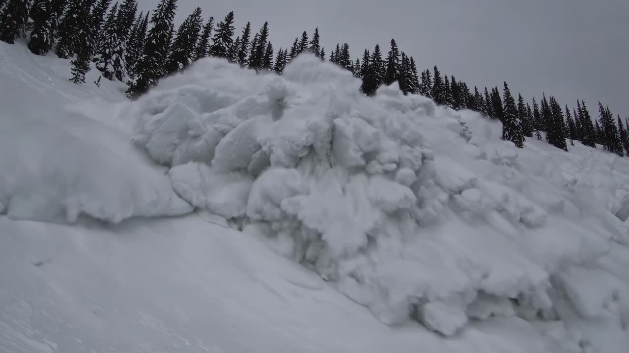 Dynamic video still of a snow avalanche descending a mountain slope, captured from a low-angle