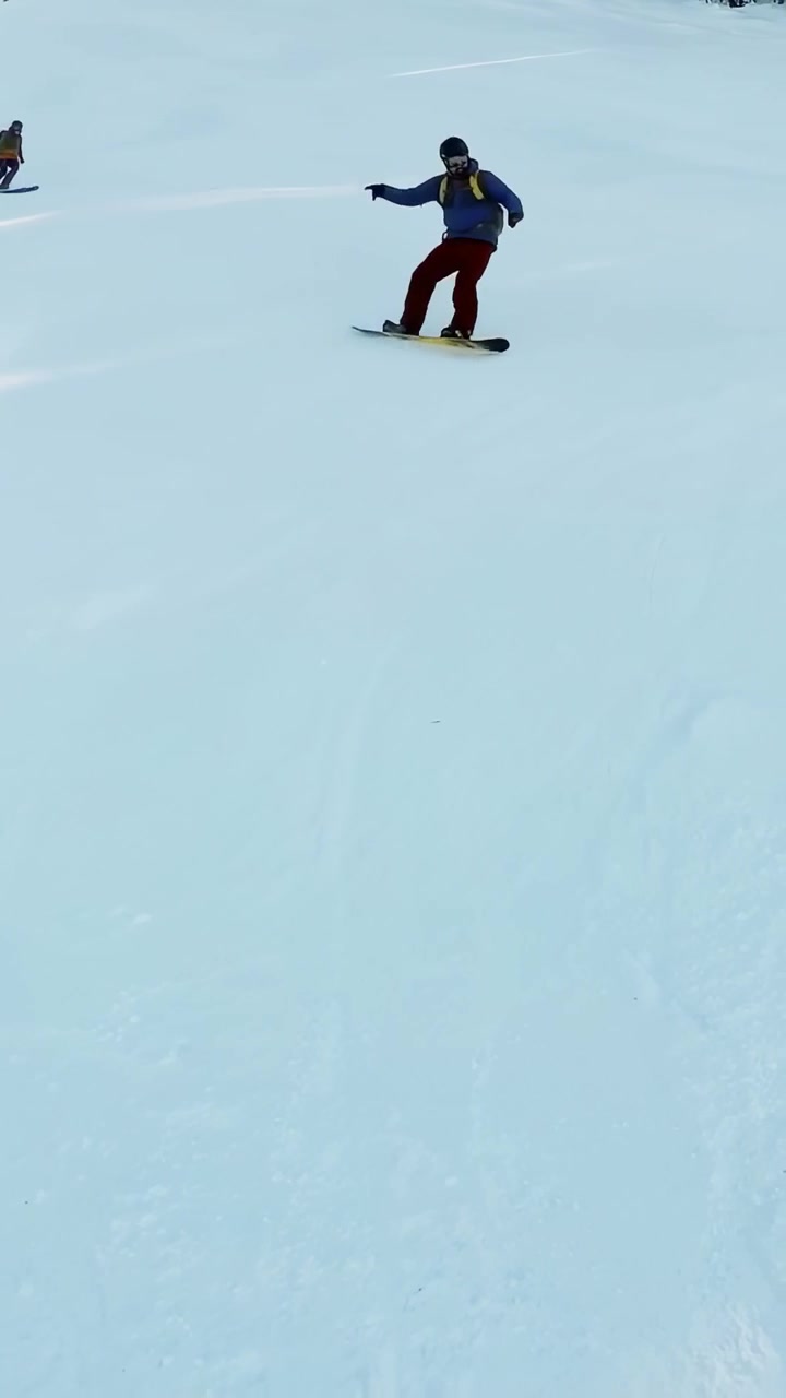Vertical video: Leaving lift skiers and boarders in turquoise pants descending run carving for fun
