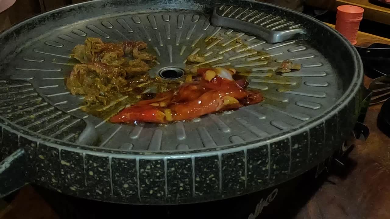 Placing meat on Korean barbecue in restaurant to grill, close up