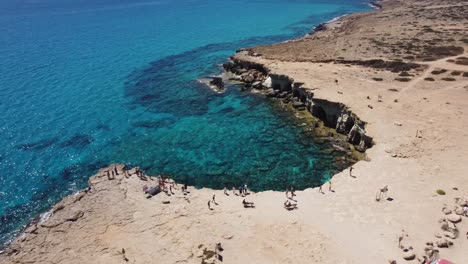 group of tourists standing on the edge of a cliff in a beautiful bay with blue water