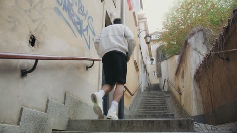 hombre cansado corriendo escaleras arriba en un callejón urbano con escaleras, tiro de seguimiento de un hombre deportivo visto desde atrás