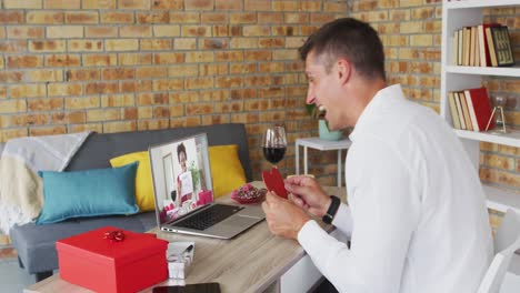 Vielfältiges-Paar-Bei-Einem-Valentinstag-Videoanruf.-Frau-Auf-Dem-Laptop-Bildschirm-Hält-Das-Schild-„Heirate-Mich“-In-Der-Hand