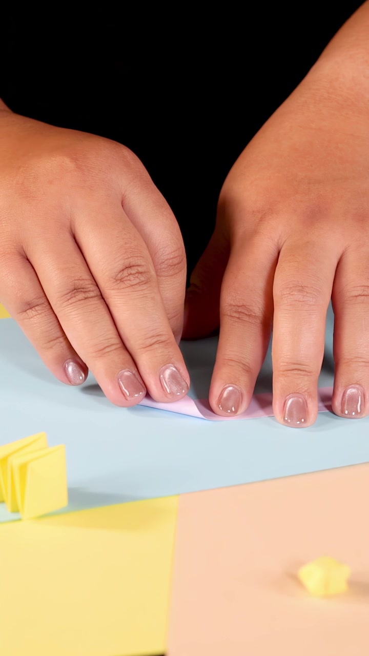 Primo piano di mani che piegano carta origami blu, fogli colorati, illuminazione brillante, telecamera fissa