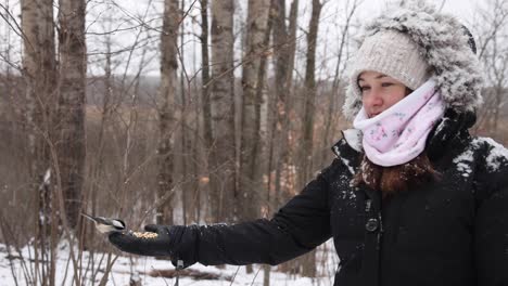 2 pájaros aterrizan en la mano de una mujer bonita para comer semillas en una caída de nieve lenta