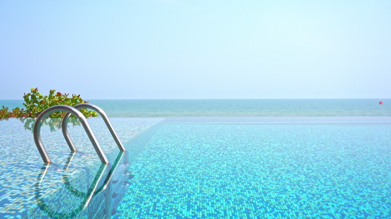 Leerer Zugang zu einem Infinity-Pool mit Metallgeländern und Meer im Hintergrund an einem wolkenlosen Tag.