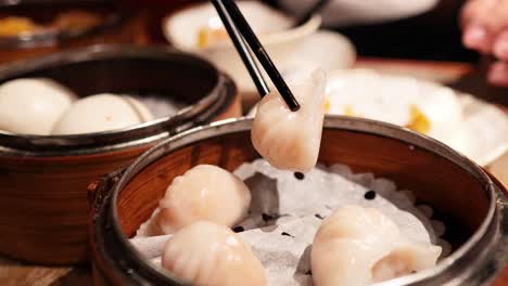 chopsticks picking dumplings from a bamboo steamer