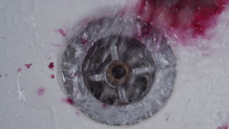 dark red liquid swirls with shower water to rinse down bath drain