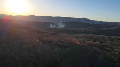 Eine-Drohnenaufnahme-In-Neuengland,-Speziell-In-Vermont,-Die-Die-Skiberge-Im-Hintergrund-Und-Eine-Rauchwolke-In-Der-Ferne-Zeigt