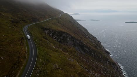 white camper van drives along a spectacular coastal road in ireland along the wild atlantic way