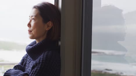 happy asian woman wearing pullover relaxing and thinking at window alone