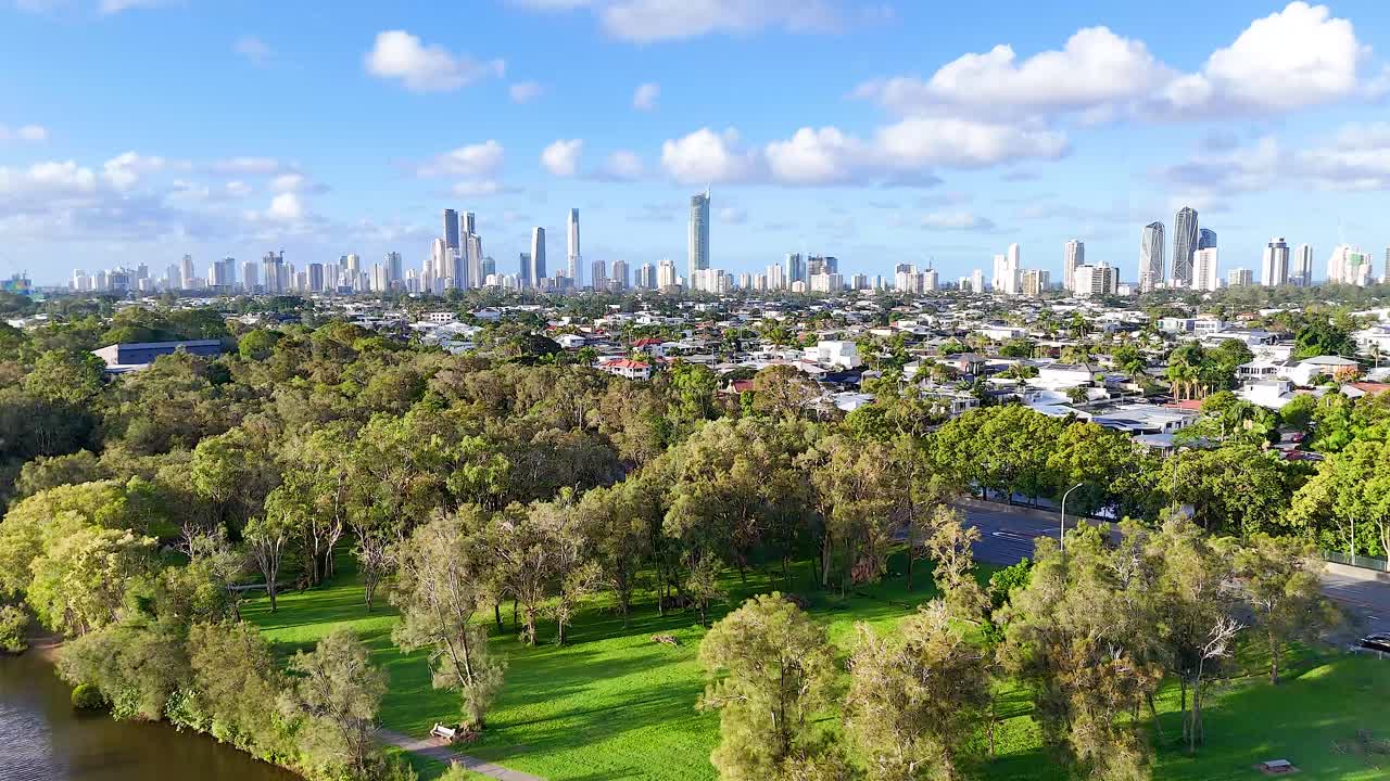 Aerial footage captures the Gold Coast skyline with lush parkland in the foreground under bright, clear skies