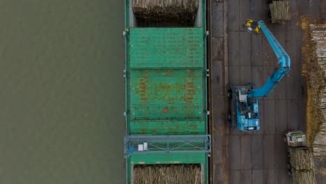 aerial birdseye view of wood terminal crane loading timber into the cargo ship, port of liepaja , lumber log export, overcast day with fog and mist, wide drone shot moving backward