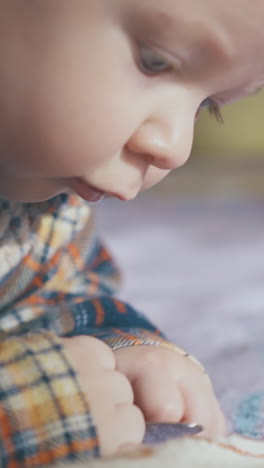adorable blond baby in bright warm shirt plays with spoon on soft bed in light room extreme close view