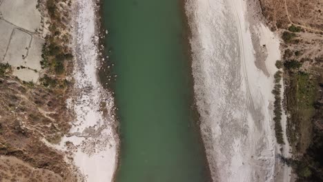 Vista-Aérea-De-Un-Río-Con-Agua-Verdosa-Que-Fluye-Entre-Bancos-Arenosos-Y-áridos-Con-Vegetación.