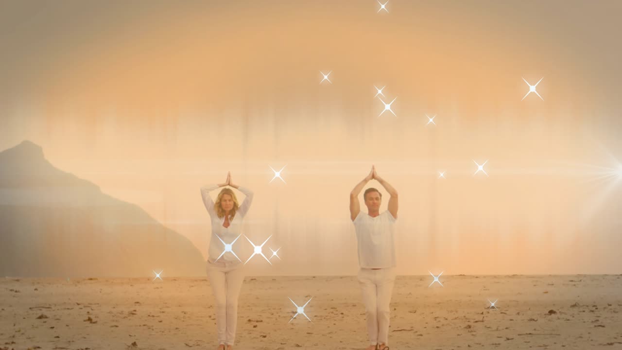 Caldo bagliore che rivela una coppia che fa yoga sulla spiaggia, scintillii che si sovrappongono, la coppia che assume la posizione dell'albero per il benessere