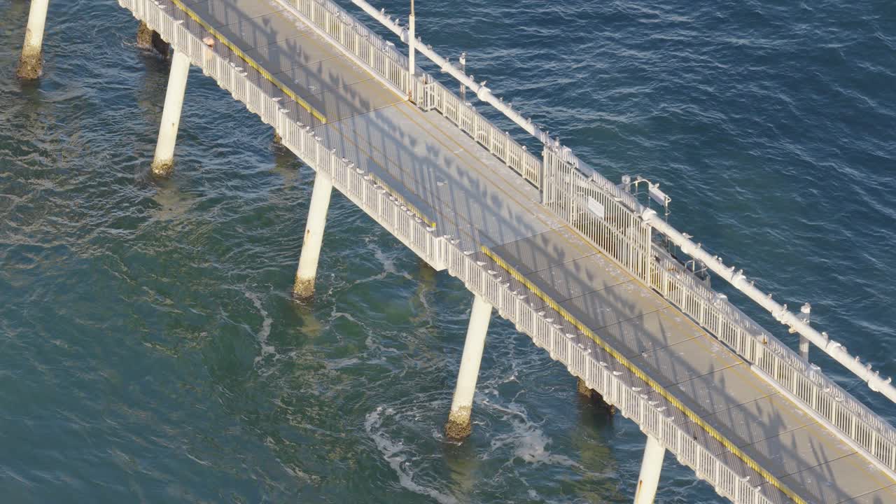 Drone footage captures a serene jetty extending over the ocean at sunset, highlighting the tranquil coastal environment