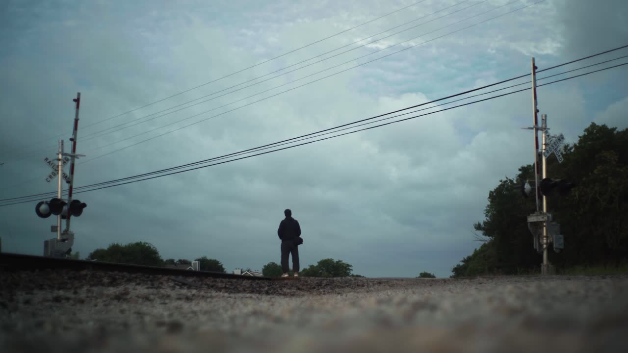 A lone person stands in the middle of train tracks, pensively looking up at the sky