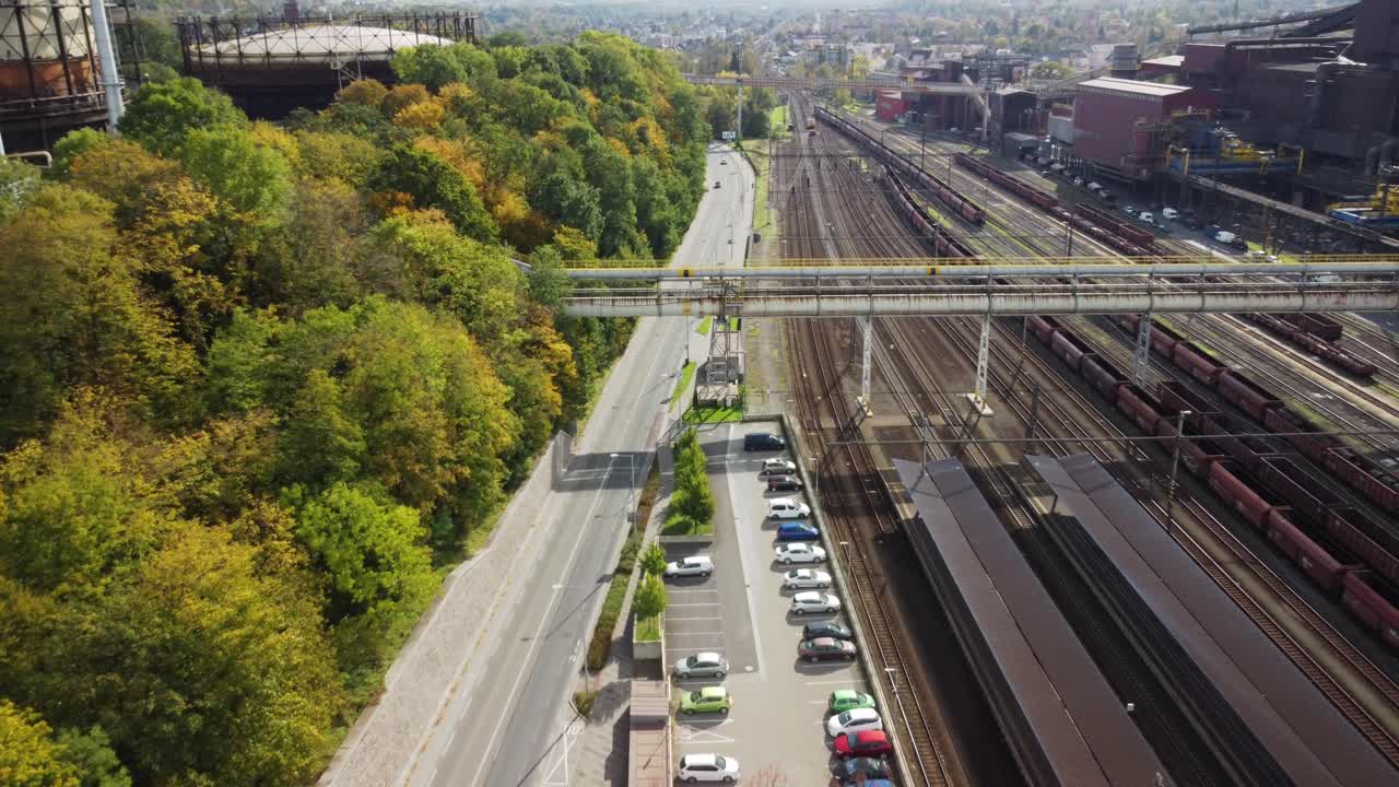 Railway lines alongside a forested road with vehicles, industrial buildings, and lush greenery