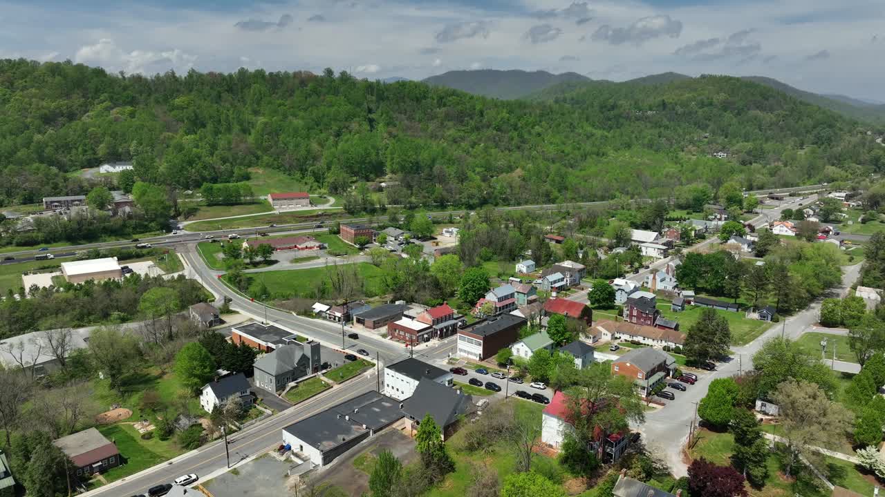 Calm green trees in small american village with traffic on interstate leading between mountains. Aerial wide shot. Historic small town in Virginia, USA. Panorama aerial view.