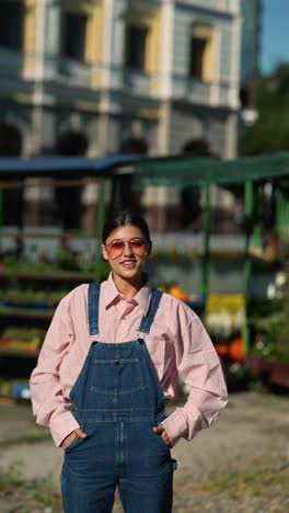 stylish woman in a pink shirt and denim overalls at a market