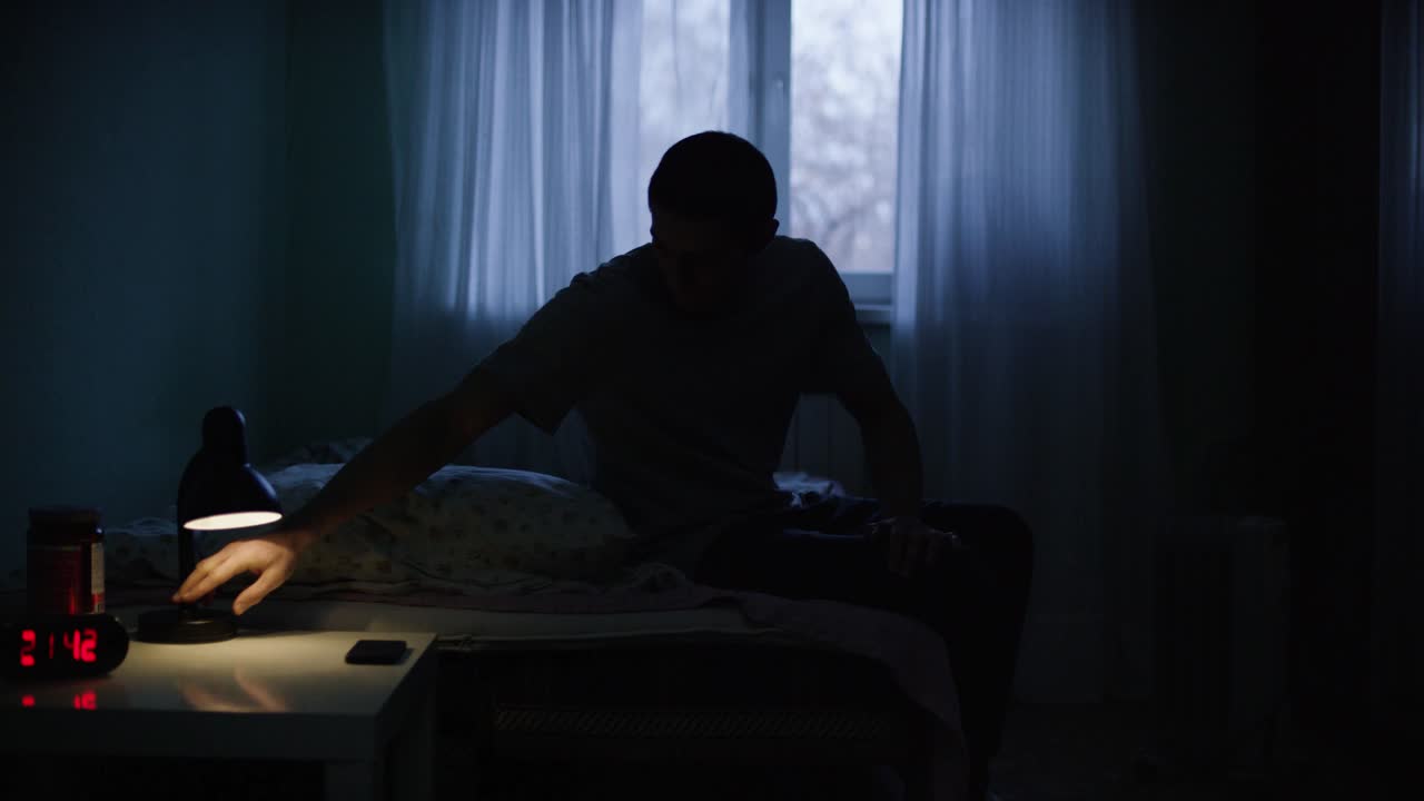 밤에 어두운 침실에 앉아있는 남자