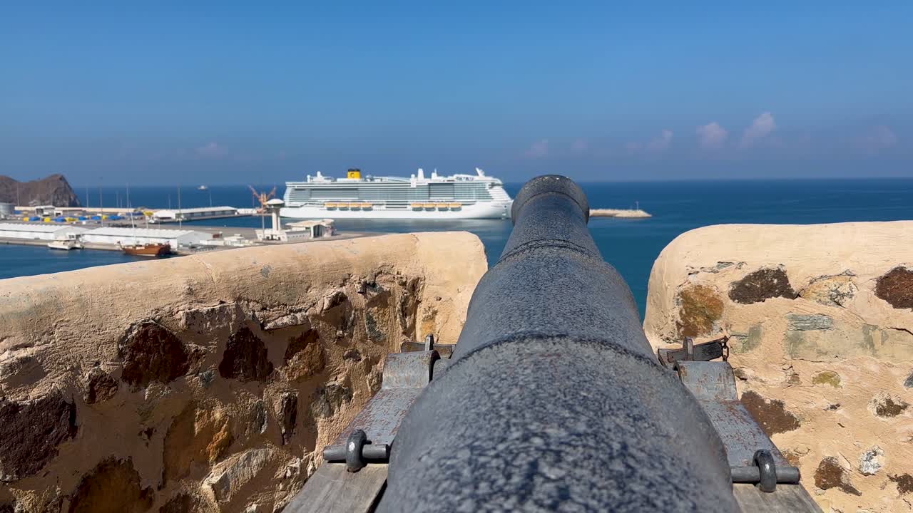 오만 만 (oman gulf) 에 있는 무트라 요새 (mutrah fort) 의 대포와 항구에 있는 크루즈 선박.