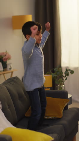 Vertical-Video-Of-Disruptive-Young-Boy-Behaving-Badly-At-Home-Jumping-On-Sofa