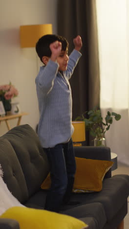 video vertical de un niño perturbador que se comporta mal en casa saltando en el sofá